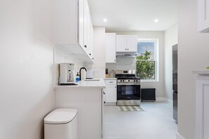 A modern kitchen with white cabinetry, a stove, oven, and a window providing a view of the outdoors.