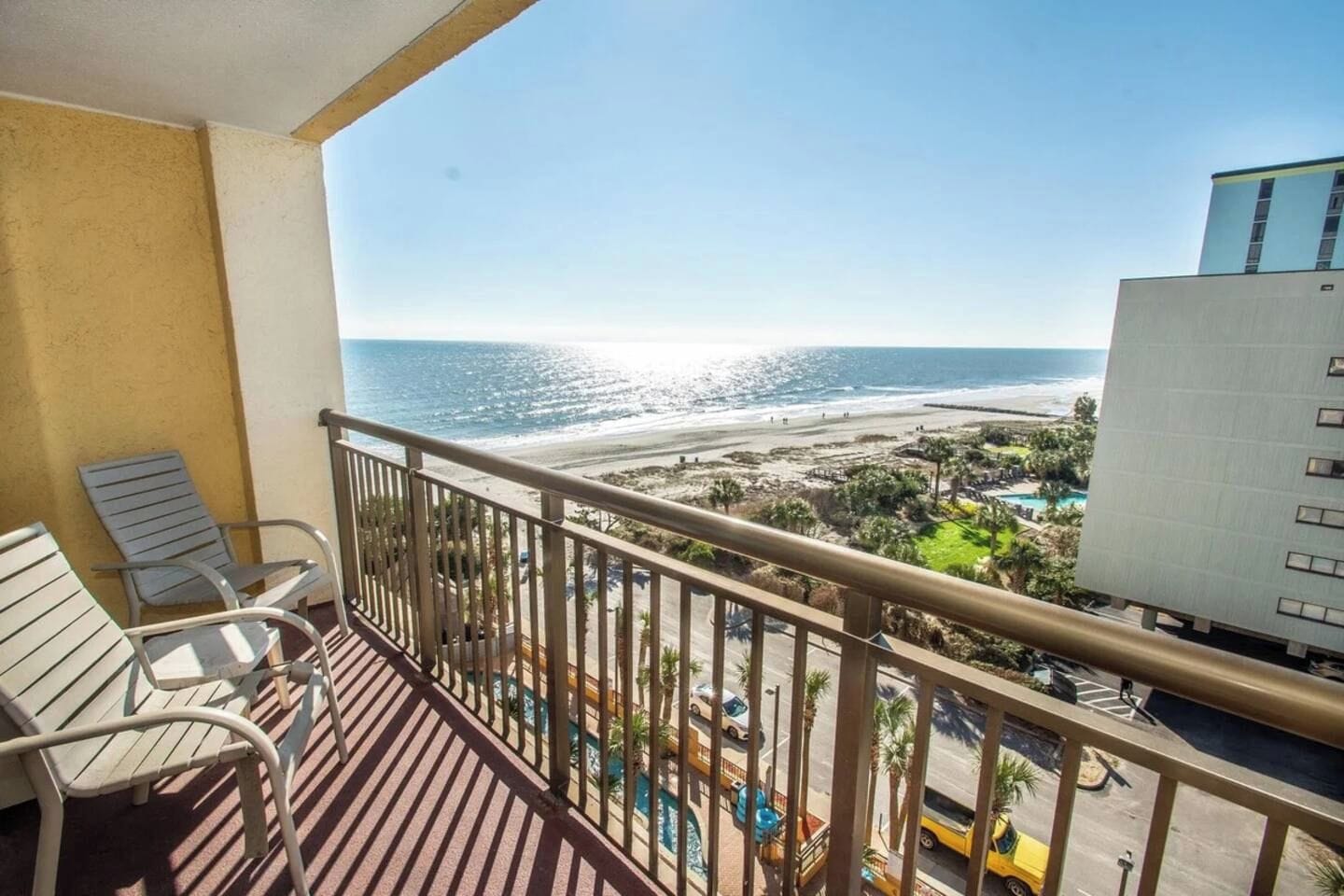 A balcony with a view of a beach and a pool area.