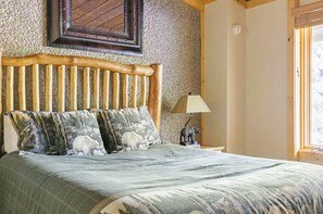 Een bed met een houten hoofdbord, meerdere kussens met dierenprinten, een lamp op een nachtkastje en een raam met uitzicht.