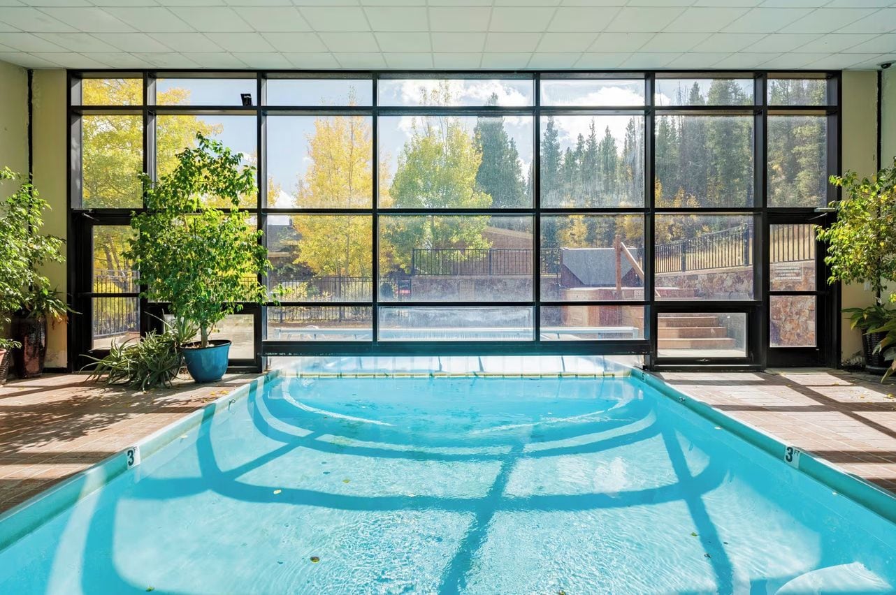 Una piscina interior con vistas a una zona boscosa a través de amplias ventanas.