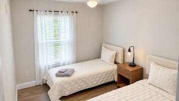 A bedroom with two beds, a ceiling fan, a nightstand with a lamp, and a window with curtains.