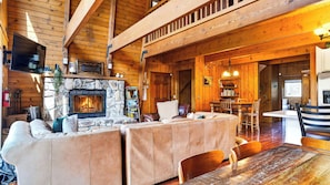 A cozy cabin interior with a stone fireplace, leather sofas, a dining area, and wooden beams. - Bear Pine Lodge by Avantstay Hot Tub + Firepit + Arcade Mountain Views Mins to Slopes + Lake (Big Bear City)