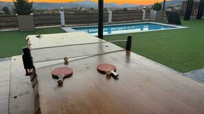 A ping pong table with two paddles and a ball, set against a backdrop of a swimming pool and a view of mountains. - Mirador el Llano 3 Pozo Alcón by Ruralidays (Province of Jaén)