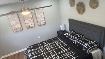 Een slaapkamer met een bed, nachtkastje, plafondventilator en wanddecoratie.