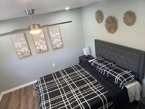 A bedroom with a bed, a nightstand, a ceiling fan, and wall art.