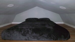 Un dormitorio con techo inclinado, una cama con cubierta oscura y suelo de madera.