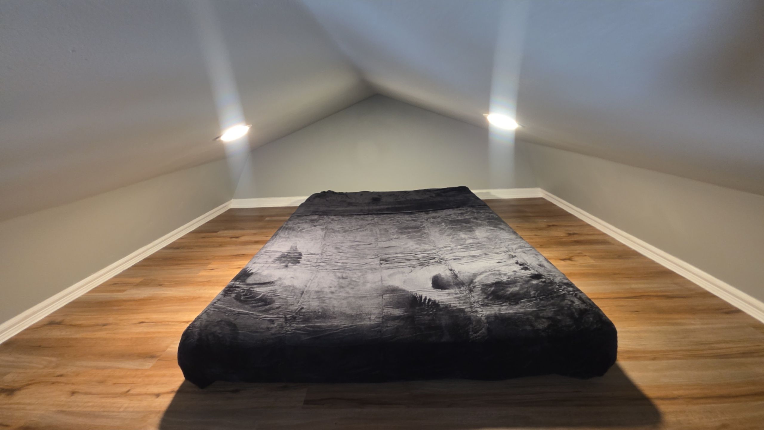 Een kamer met een bed in het midden, houten vloeren en twee plafondlampen.