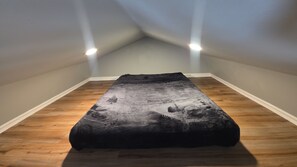 A room with a bed in the center, wooden flooring, and two ceiling lights.