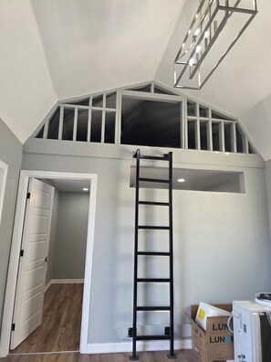 A loft bedroom with a sloped ceiling, a ladder, a door, and a box labeled 'LUNAR'.