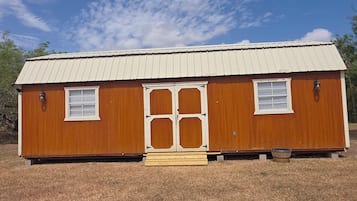 Un pequeño edificio de madera de un piso con techo metálico, dos ventanas y una puerta central.