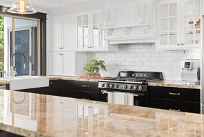 A modern kitchen with white cabinetry, a black stove, and a marble countertop. - Waterfront 5BR + Pool | Kawana Island | Sleeps 10 (Parrearra)