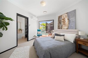 A bedroom with a large bed, a view to the outside, a chair, and a painting on the wall. - Waterfront 5BR + Pool | Kawana Island | Sleeps 10 (Parrearra)