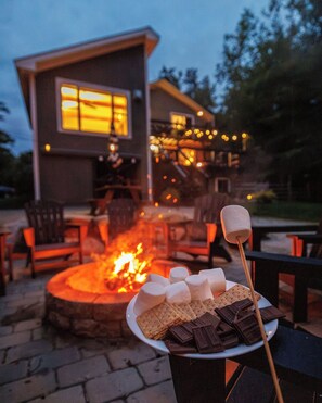 A cozy outdoor seating area with a fire pit, a plate of marshmallows, and chocolate bars. - Cozy Lakefront home in the heart of the White Mountains (Conway)