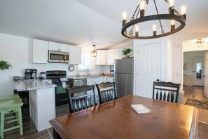 A modern kitchen with white cabinets, a stainless steel refrigerator, a built-in microwave, and a coffee station.