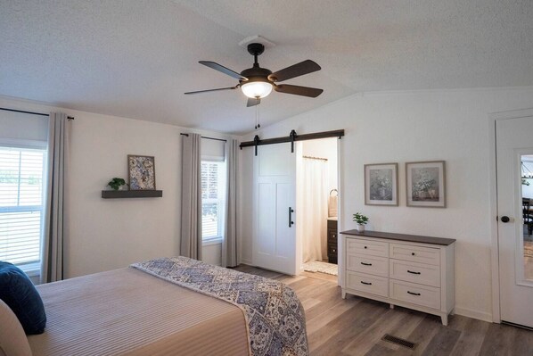Un dormitorio con cama, cómoda, ventilador de techo y ventana.