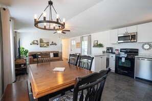 Una cocina moderna con zona de comedor, que incluye una mesa de madera, sillas, una lámpara de araña y electrodomésticos empotrados.