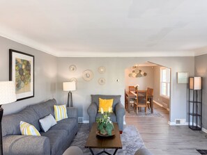 A living room with a grey sofa, a coffee table with a plant, and a dining area with a wooden table and chairs. - Large 4-bedroom townhome with AC walking distance from DMC Sinai Grace Hospital (Detroit)