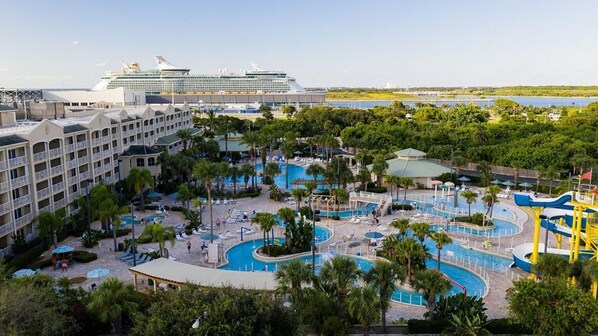 A resort with multiple swimming pools, a large cruise ship in the background, and lush greenery. - Oceanfront 2BR Villa at Cape Canaveral Beach Resort – Space & Sun (Cape Canaveral)