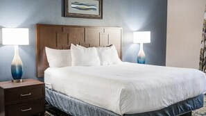 A hotel room with a large bed, two bedside tables with lamps, a wooden headboard, and a framed picture on the wall. - Oceanfront 2BR Villa at Cape Canaveral Beach Resort – Space & Sun (Cape Canaveral)