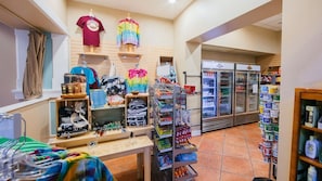 A retail store with clothing racks, shelves with various products, and a refrigerated display case.