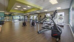 A spacious gym with cardio machines, mirrors, and a wooden floor.