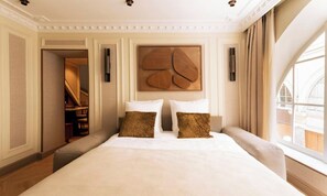 A hotel room with a large bed, two pillows, a wooden headboard, a view of the outside, and a staircase leading to a balcony. - JUST MOMENTS FROM THE LOUVRE, OPÉRA GARNIER & GRANDS BOULEVARDS (Paris)