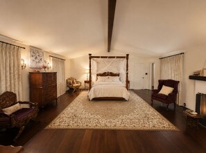 Une chambre spacieuse avec un lit à baldaquin, une commode en bois, une chaise longue et un grand tapis.