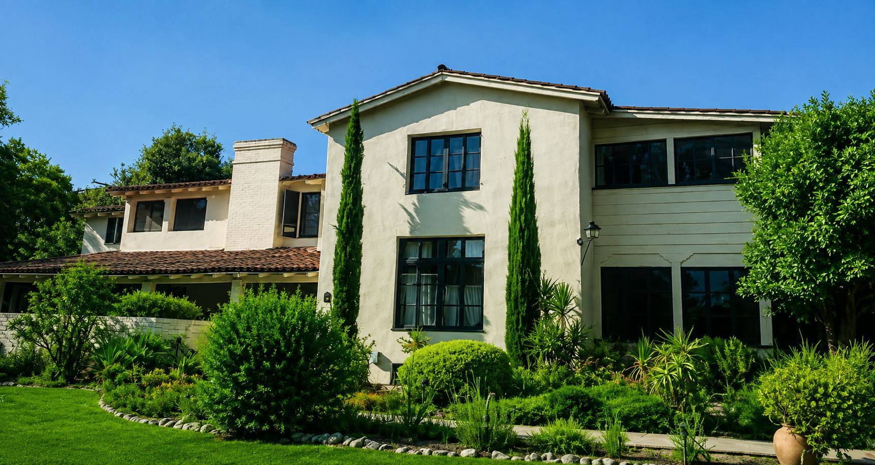 A two-story house with a well-maintained garden, a stone wall, and a clear blue sky.