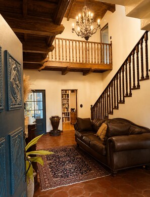 A spacious living area with a leather sofa, a chandelier, a staircase, and a bookshelf. - Spacious 5-bedroom house in peaceful Monrovia with AC and gym (Monrovia)
