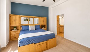 Ein Schlafzimmer mit einem großen Bett, einem Holzkopfende, Nachttischen und Blick in die Küche.