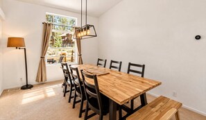 Ein Essbereich mit einem Holztisch, sechs Stühlen, einer Stehlampe und Blick auf ein Haus durch ein Fenster.