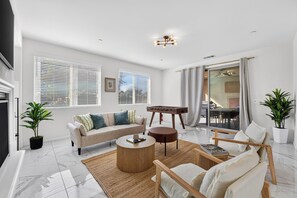 A modern living room with a sofa, coffee table, and chairs, a foosball table, and large windows with blinds.