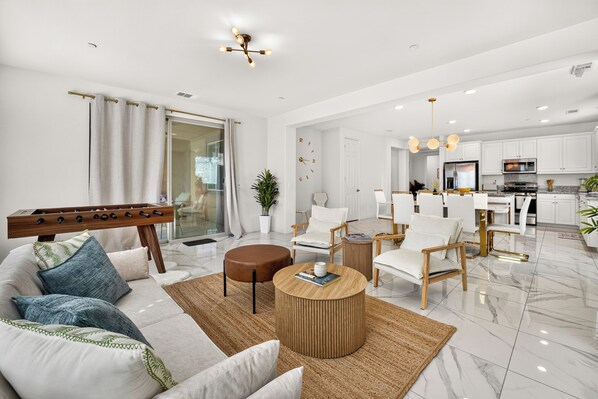A modern living room with a sofa, coffee table, and chairs, a dining area with a table and chairs, and a kitchen with appliances.