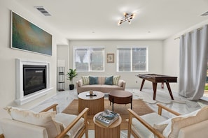 A spacious living room with a fireplace, a sofa set, a coffee table, and a foosball table.