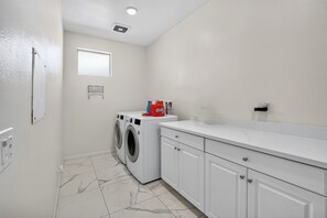 A laundry room with a washing machine, a dryer, and a countertop with a red detergent bottle.