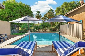 Piscina com duas espreguiçadeiras e dois guarda-sóis.