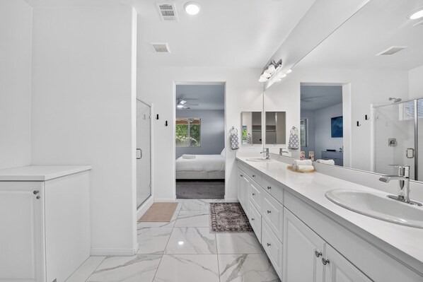 A modern bathroom with a large mirror, a walk-in shower, and a separate bedroom with a bed.