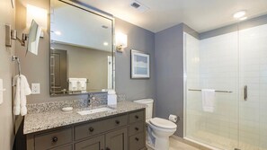 Un baño moderno con encimera de granito, un espejo grande, un inodoro y una cabina de ducha con mampara de vidrio.
