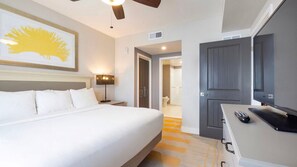 Habitación de hotel con cama, escritorio con computadora, ventilador de techo y puerta que da a un baño.