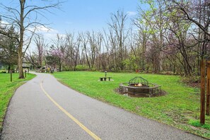 A paved pathway leading through a park with a fire pit and benches. - Charming Winona Lake Cottage Near Trails & Village (Winona Lake)