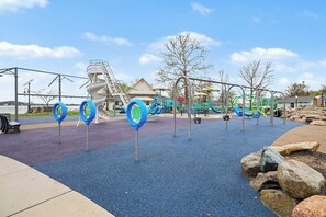 A playground with various play equipment, including swings and slides, set against a backdrop of trees and a building. - Charming Winona Lake Cottage Near Trails & Village (Winona Lake)