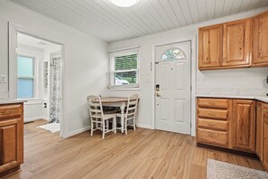 A kitchen with wooden cabinets, a white door, and a dining table with chairs. - Charming Winona Lake Cottage Near Trails & Village (Winona Lake)