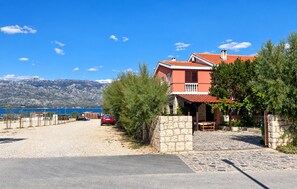A coastal property with a stone driveway, a red car parked in front, and a view of the sea and mountains in the background. - Gorgeous apartment in Razanac with house sea view (Razanac)