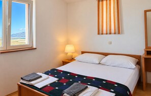 A bedroom with a bed, a nightstand with a lamp, a window with a view, and a quilt on the bed. - 2 bedroom nice apartment in Razanac (Razanac)
