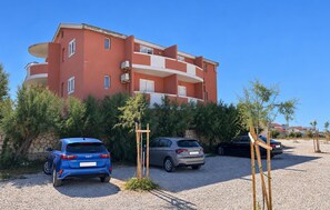 Ein mehrstöckiges Wohngebäude mit roter Fassade, einem Parkplatz mit Kiesbelag und mehreren parkenden Autos.