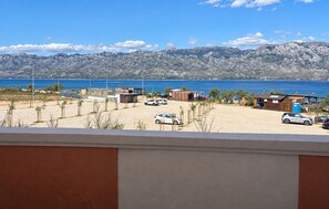 Vista costeira com área de estacionamento, instalações de praia e montanhas ao fundo.