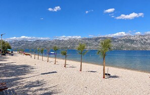 Ein Kiesstrand mit Bäumen und einer Bergkulisse.