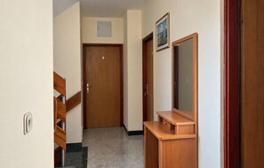 Um corredor com uma porta de madeira, um espelho e um pequeno quadro na parede.