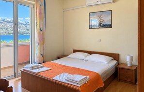 Una camera d'albergo con un letto, un comodino, una lampada, un quadro appeso al muro e vista mare dalla finestra.