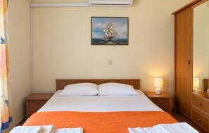 Ein Hotelzimmer mit einem Bett, einem Nachttisch, einer Lampe, einem Schiffsbild an der Wand und einem Kleiderschrank.